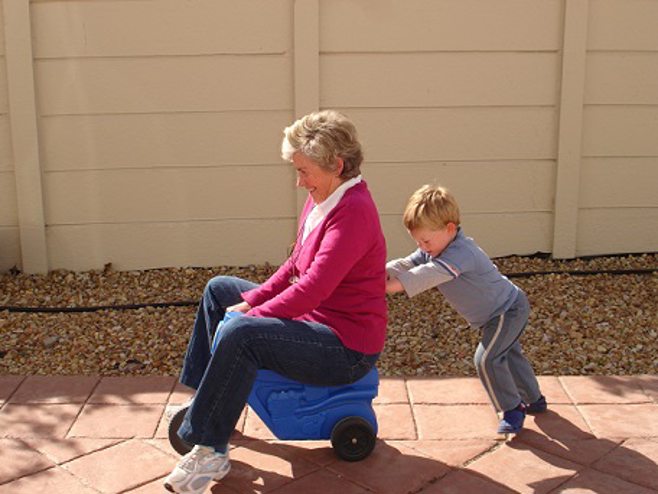 Child pushing grandma on plastic toy car. Child pushing grandma on plastic toy car.